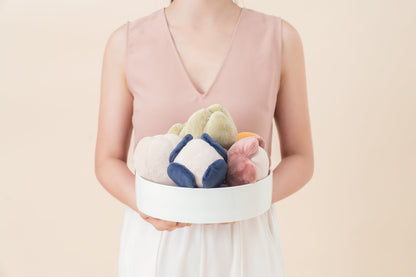 Person holding a white box with colorful plush toys against a light pink background