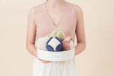 Person holding a white box with colorful plush toys against a light pink background