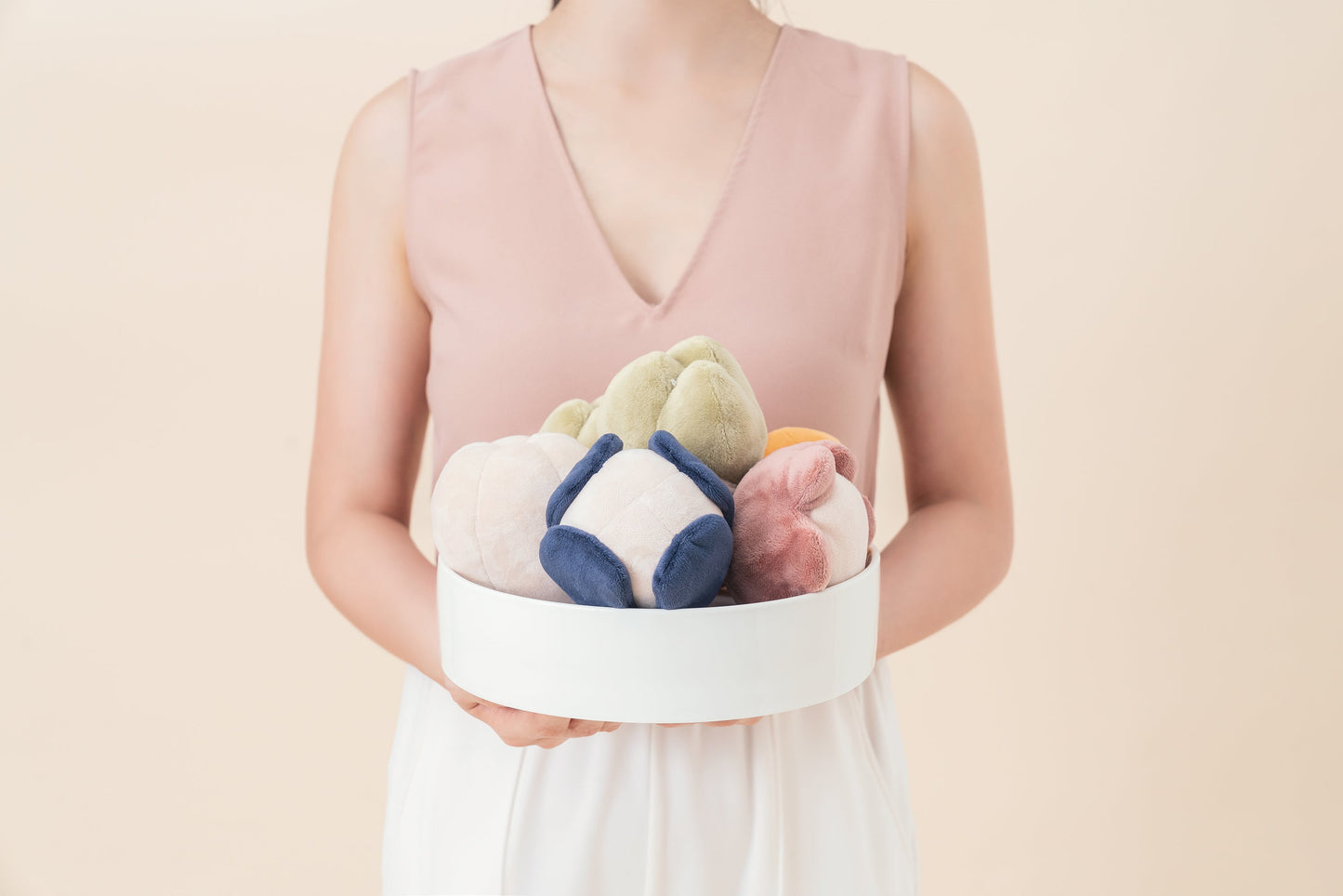 Person holding a white box with colorful plush toys against a light pink background
