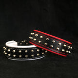 Two leather dog collars with studs, one black and white, one black and red, on a black background.
